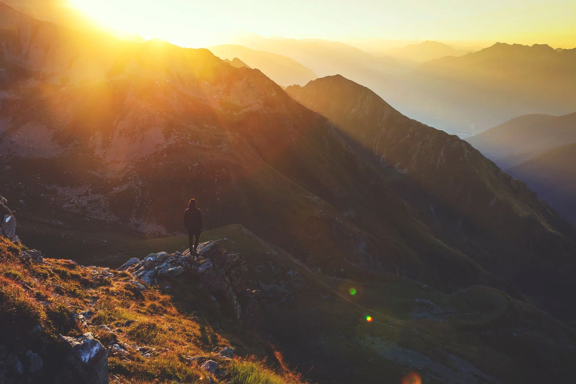Soft sunrise light over a mountain ridge, with a lone hiker on the trail below